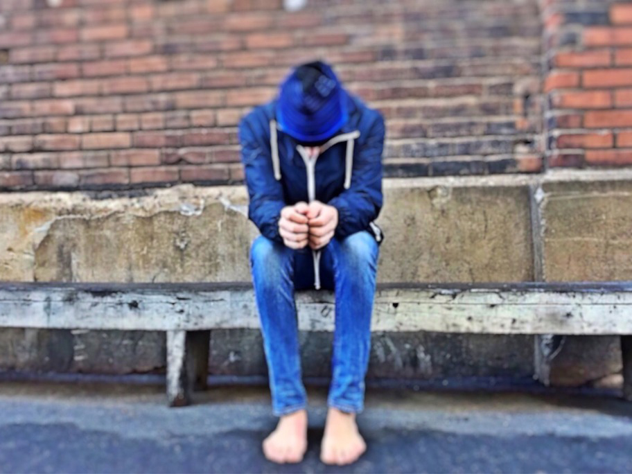 Boy sitting on bench with head bowed down