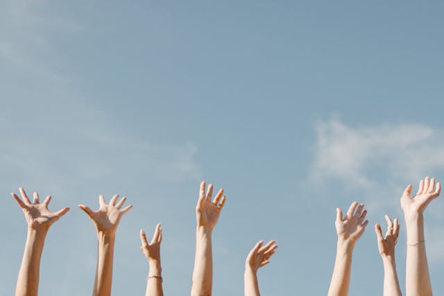 Several hands are raised into the air with a clear sky as a backdrop.