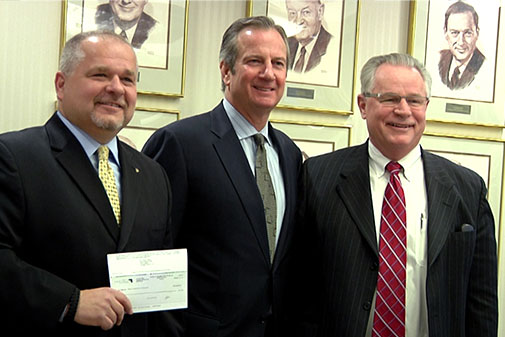 Three men standing together, holding a check